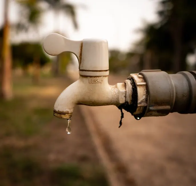 A close-up shot of a water droplet falling from an outdoor tap, highlighting water conservation issues.